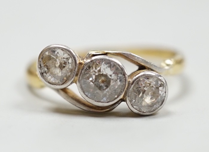 A yellow metal and three stone diamond set crossover ring, size N/O, gross weight 3.1 grams.